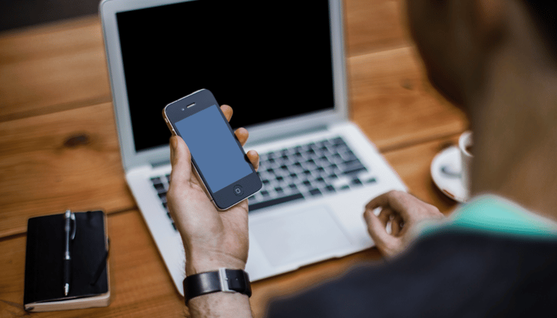 Person holding a smartphone in front of a laptop